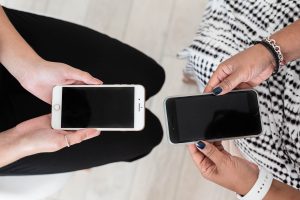 Two women seated holding phones with black screen facing up