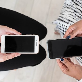 Two women seated holding phones with black screen facing up